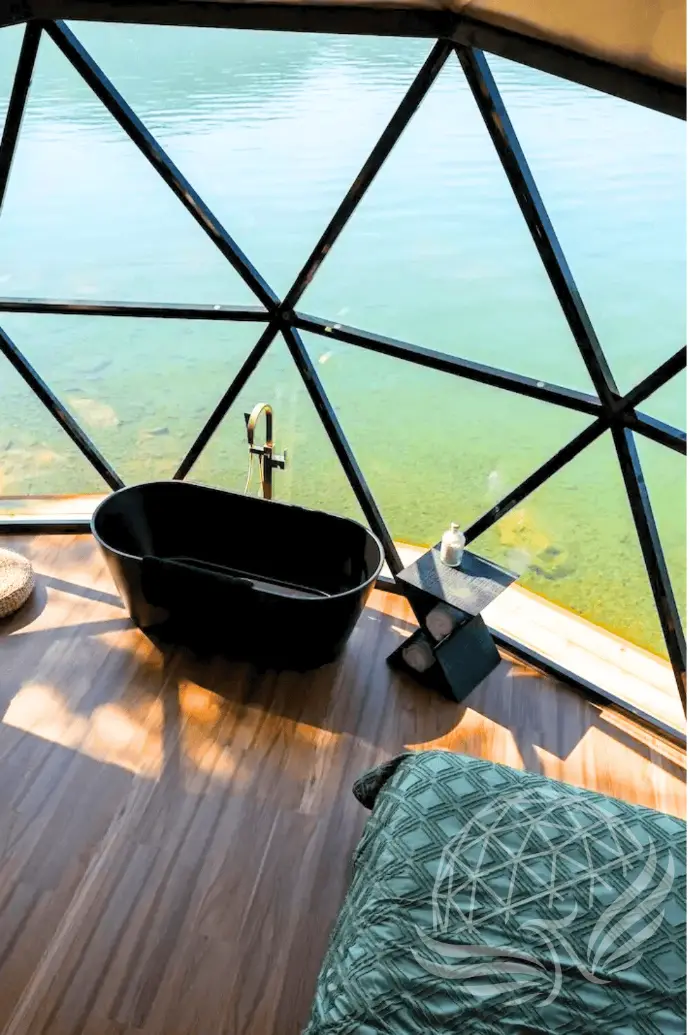 a bath tub and bed in front of a hybrid panorama window overseeing a lake