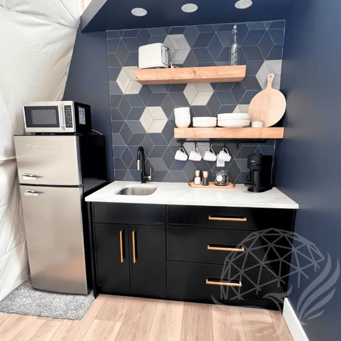 a mini kitchen with sink, ref, microwave and amenities inside a geodesic dome