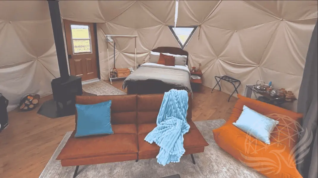 Interior of the glamping dome at Worthwhile Escape in Alberta, Canada, featuring a queen bed, wood-burning stove, modern seating, and rustic comforts for a stylish and serene off-grid stay.