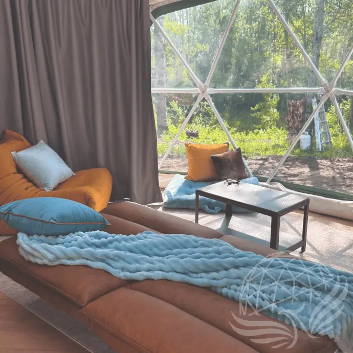 Lounge area inside the Worthwhile Escape glamping dome in Alberta, with floor seating, plush pillows, and a full bay window overlooking forest and farmland views.