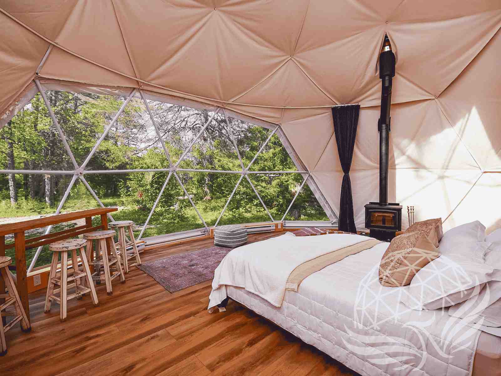 Rustic dome bedroom with wood stove and lush green forest outside