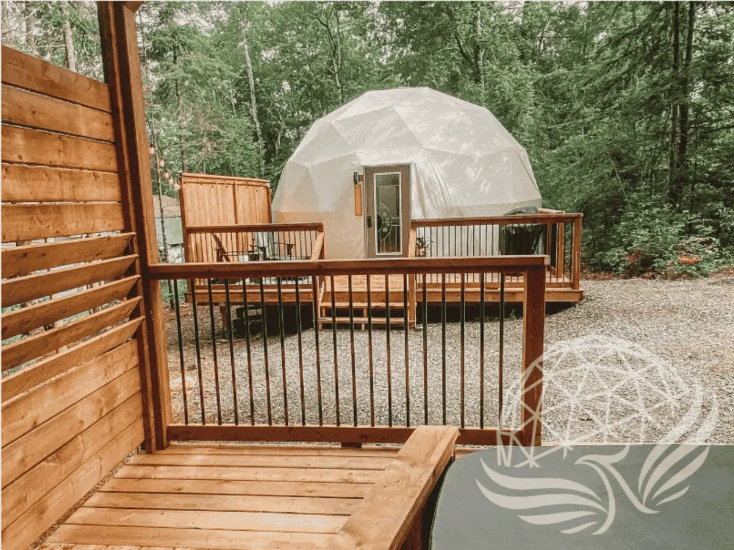White geodesic dome with wooden deck at Moonshine Dome Retreat in forest setting