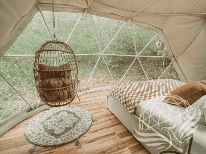 Interior view of a Moonshine Dome Retreat with hanging chair, scenic forest backdrop, and cozy bed