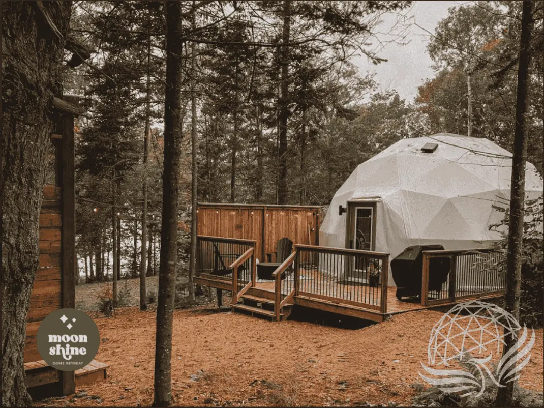 Moonshine Dome Retreat with white geodesic dome and wooden deck in forest setting