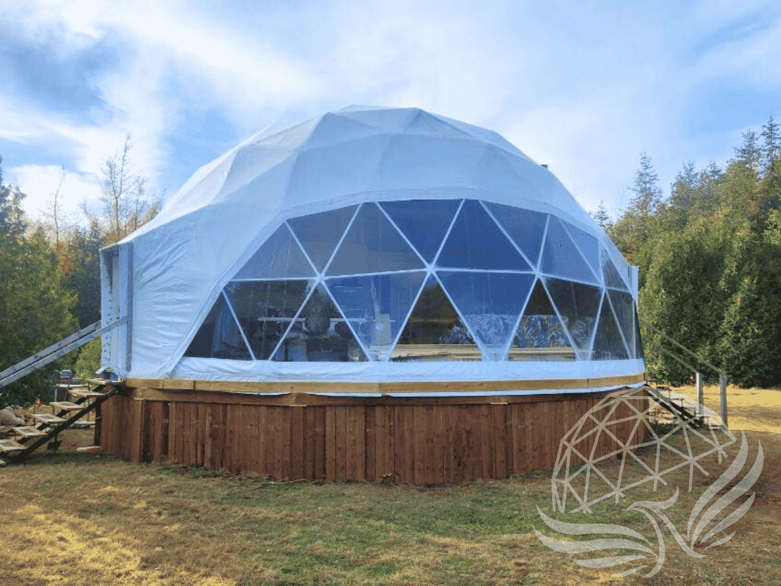 Large geodesic dome with panoramic windows elevated on a wooden platform, set in a clearing among tall evergreens.
