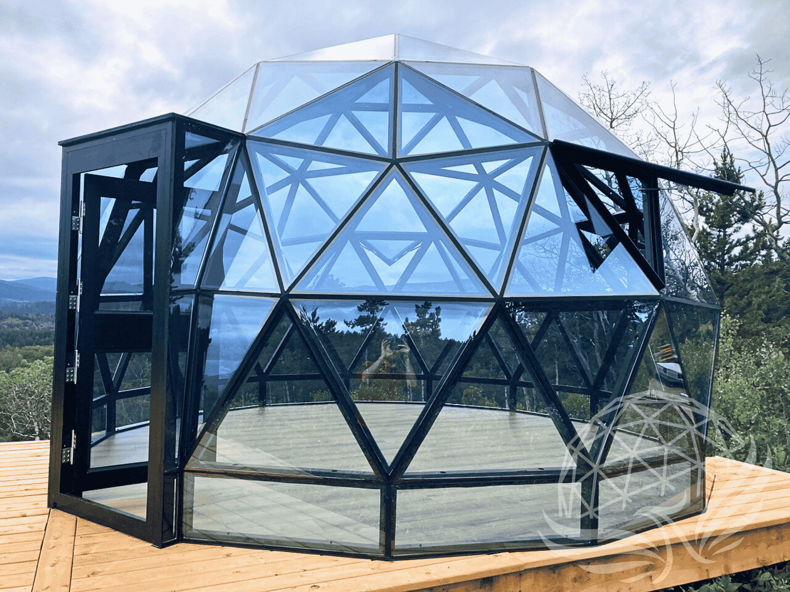 Panoramic mountain view behind a Phoenix Domes glass geodesic dome on a wooden deck.