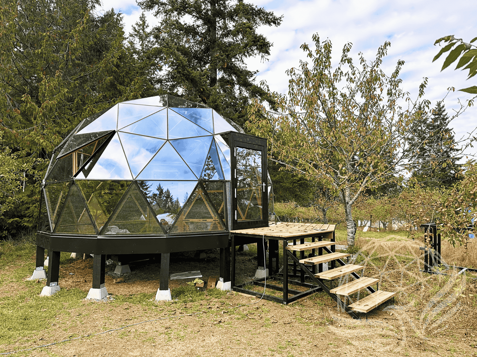 Phoenix Domes glass geodesic dome with attached wooden deck and stairs in an orchard landscape.